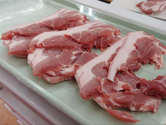 Several cuts of pork belly on a pale green tray.