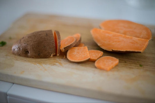 A sweet potato sliced into different-sized pieces on a wooden cutting board.