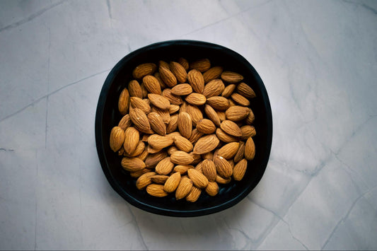 A black bowl full of almonds sits on a white surface.