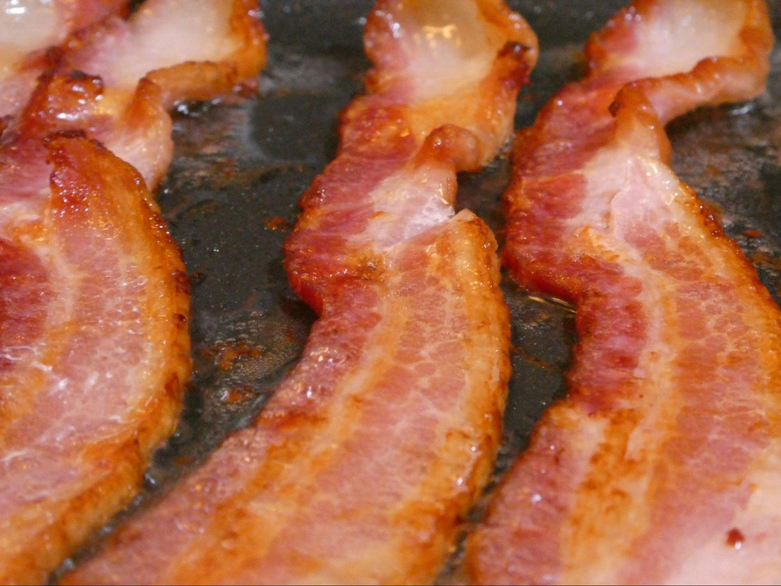 Three slices of bacon frying in a pan.